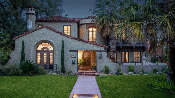A Mediterranean-style house with a stone facade, arched windows, and a well-lit entrance.