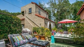 A patio with two lounge chairs, a red umbrella, and a stone building in the background.