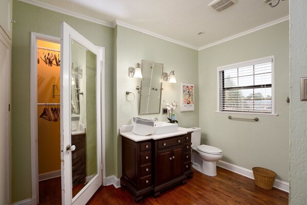 A bathroom with a vanity, a toilet, a window with blinds, and a mirror.