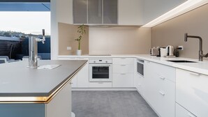 Une cuisine moderne avec des meubles blancs, un four encastré, un grand îlot central doté d’un évier et une vue sur l’extérieur.