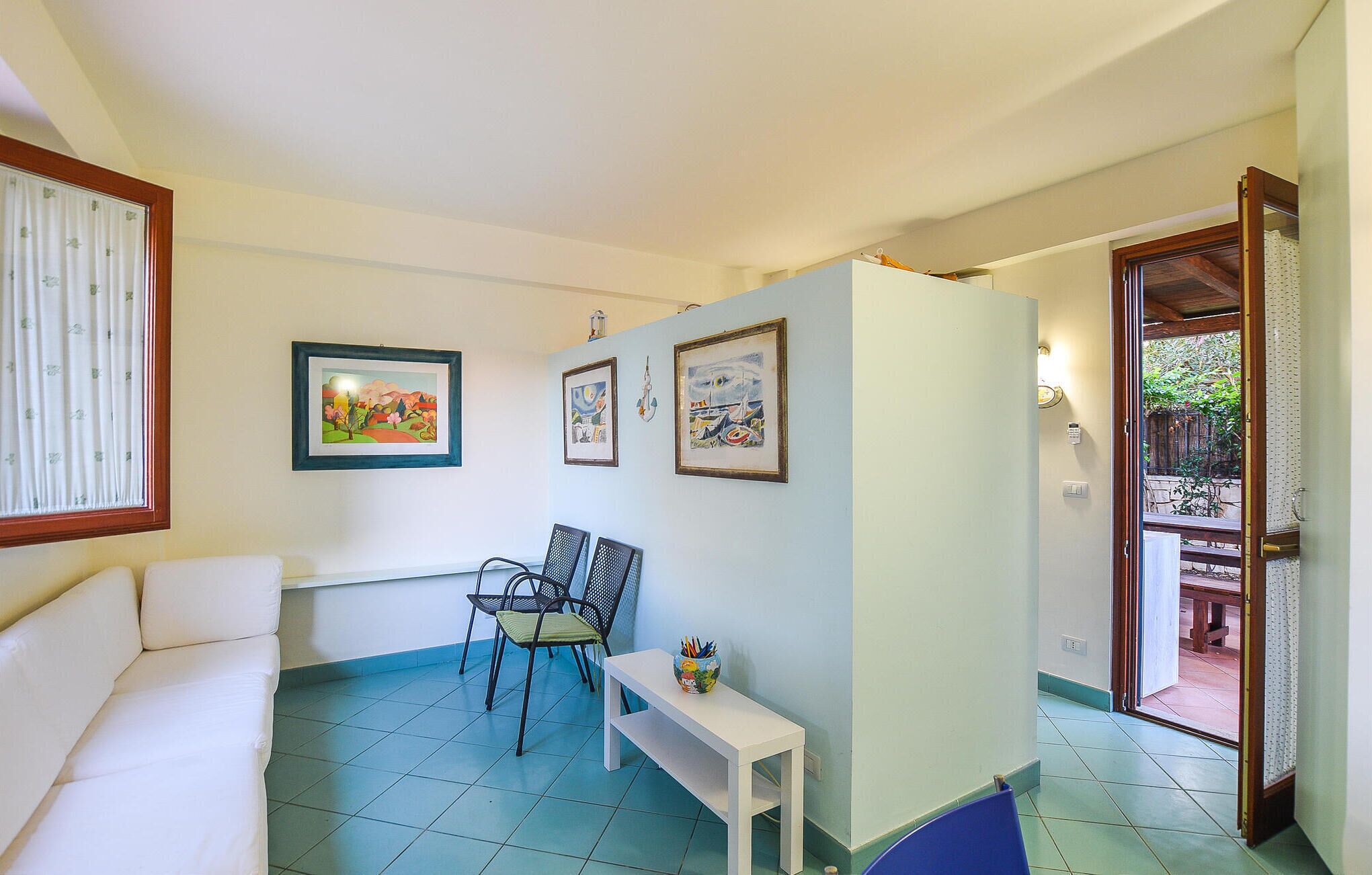Una habitación con un sofá blanco, una mesita pequeña y dos sillas. Se observan tres cuadros en la pared.