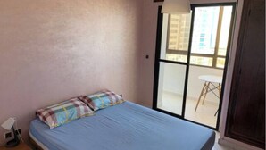 Une chambre à coucher avec un lit, une fenêtre et une vue sur un balcon équipé d’une table et de chaises.