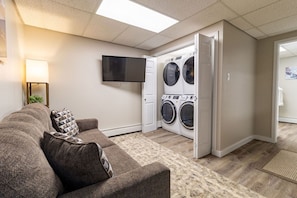 A laundry room with a washing machine and dryer, a flat-screen TV, and a couch with patterned cushions.