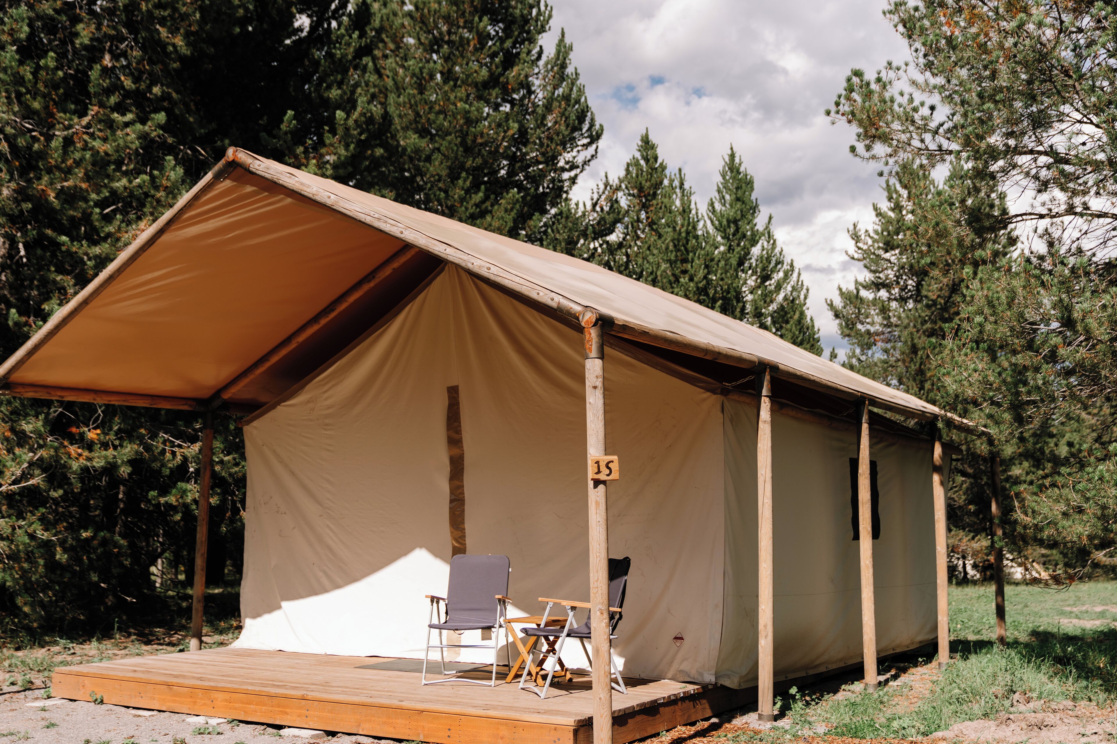 A tent with a wooden deck and two chairs, surrounded by trees.