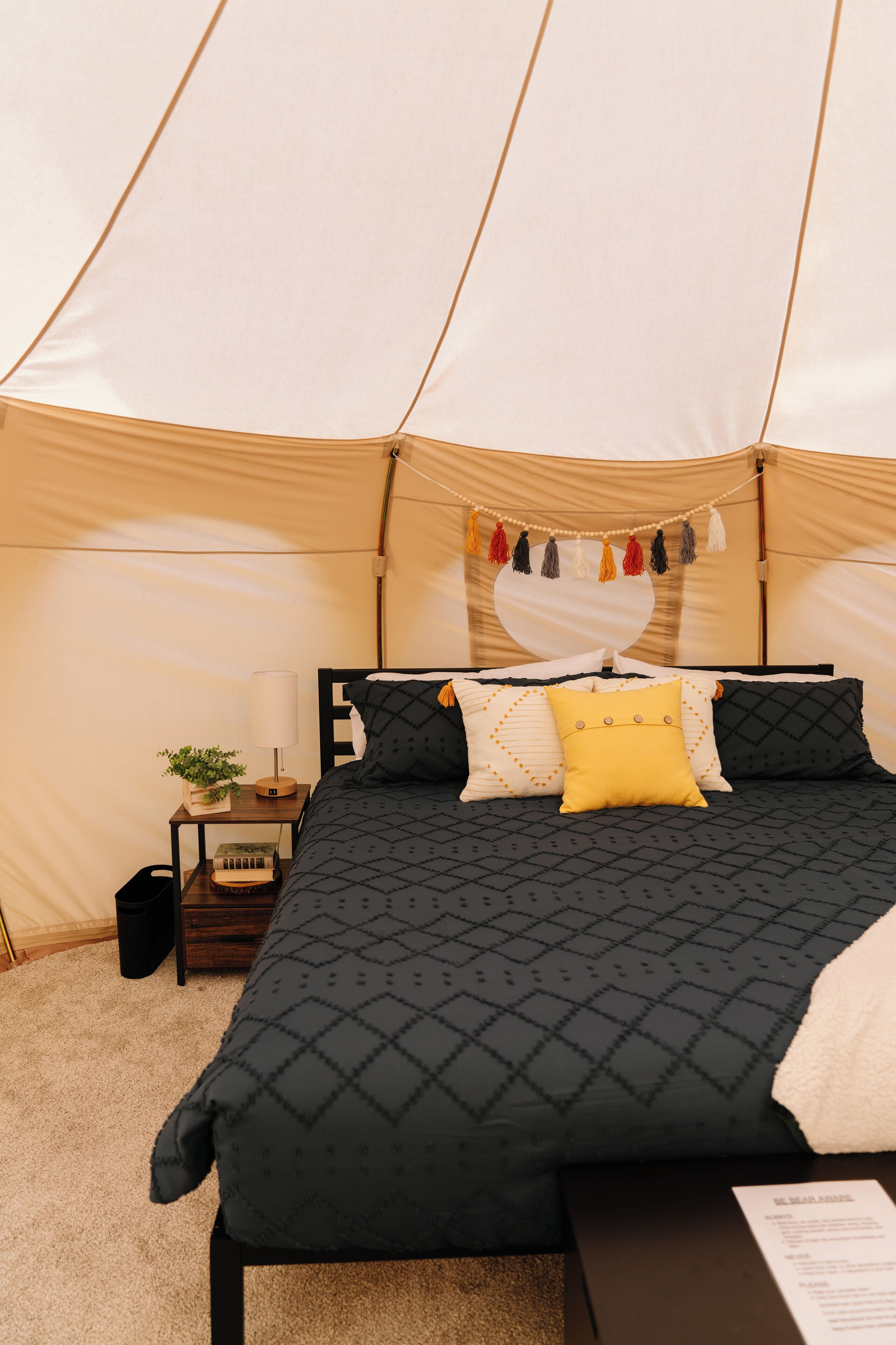 Un alloggio in tenda con un letto, cuscini, un tavolino con una lampada e una pianta.