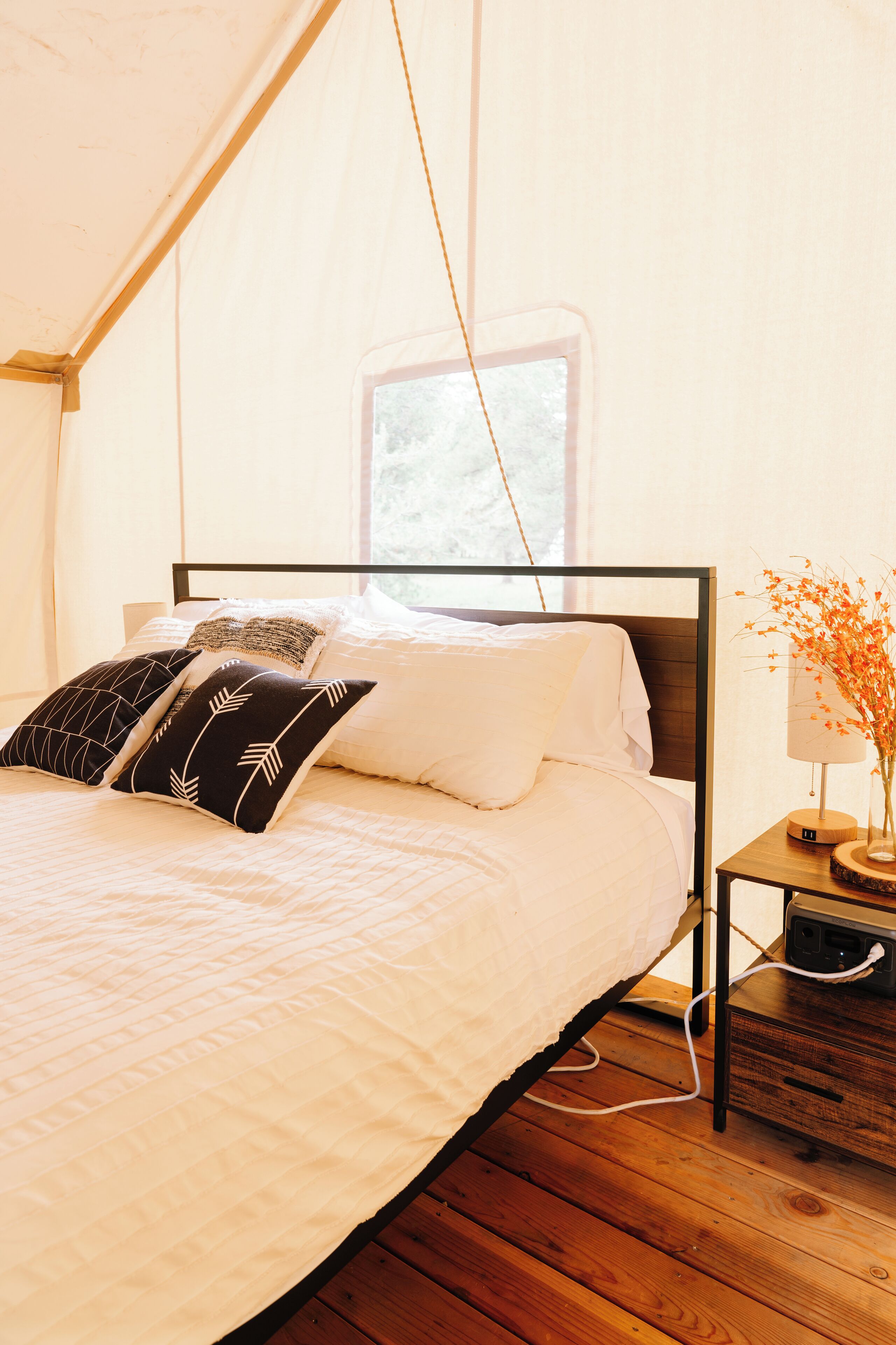 Une chambre à coucher avec un lit, des oreillers, une table de chevet avec une lampe et une fenêtre.