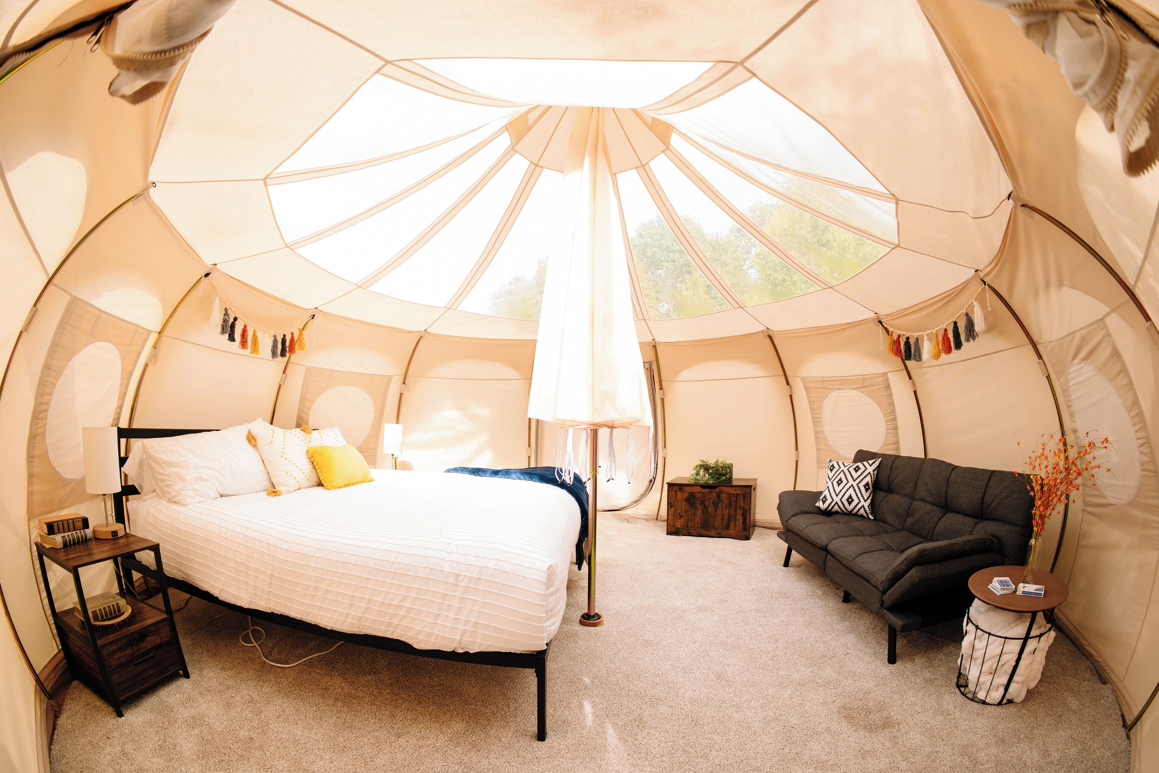 A tent with a bed, a sofa, a lamp, and a small table.
