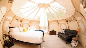 A tent with a bed, a sofa, a lamp, and a small table.