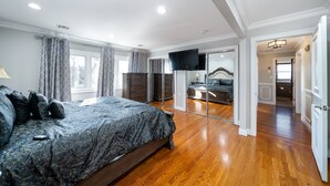 Une chambre spacieuse avec un grand lit, un téléviseur fixé au mur et un plancher en bois.