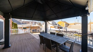 Une terrasse extérieure couverte, avec une table et des chaises, une clôture blanche et une vue sur les maisons voisines.