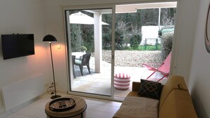 Un salon comprenant un canapé, une table basse, un téléviseur fixé au mur et une porte-fenêtre coulissante donnant sur une terrasse extérieure.