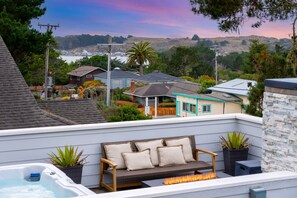 A rooftop patio with a sofa, a hot tub, and a fire feature.