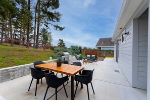 An outdoor patio with a wooden table and chairs, a barbecue grill, and a sofa with cushions.