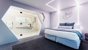 Et moderne soveværelse med et unikt geometrisk loftdesign, en stor seng med blåt sengetøj og udsigt til et badevrelse gennem et glasafskærmning.