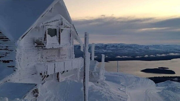 A snow-covered building with icicles, a clear sky, and a distant view of mountains and a lake. - CERRO CATEDRAL SCHUSS ARG41 (San Carlos de Bariloche)