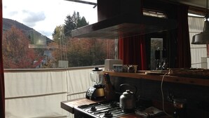 A kitchen with a stove, kettle, and blender on the counter, a window with a view of trees and mountains, and a red curtain. - CERRO CATEDRAL SCHUSS ARG41 (San Carlos de Bariloche)