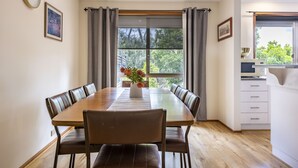 Un comedor con una mesa de madera, sillas acolchadas, un jarrón con flores y vistas a árboles a través de una ventana.