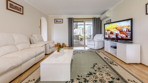 Una sala de estar con un sofá color beige, una mesa de centro blanca, un televisor de pantalla plana y un tapete estampado.