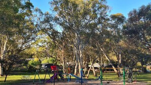 Un parque con juegos infantiles, mesas de picnic y árboles.