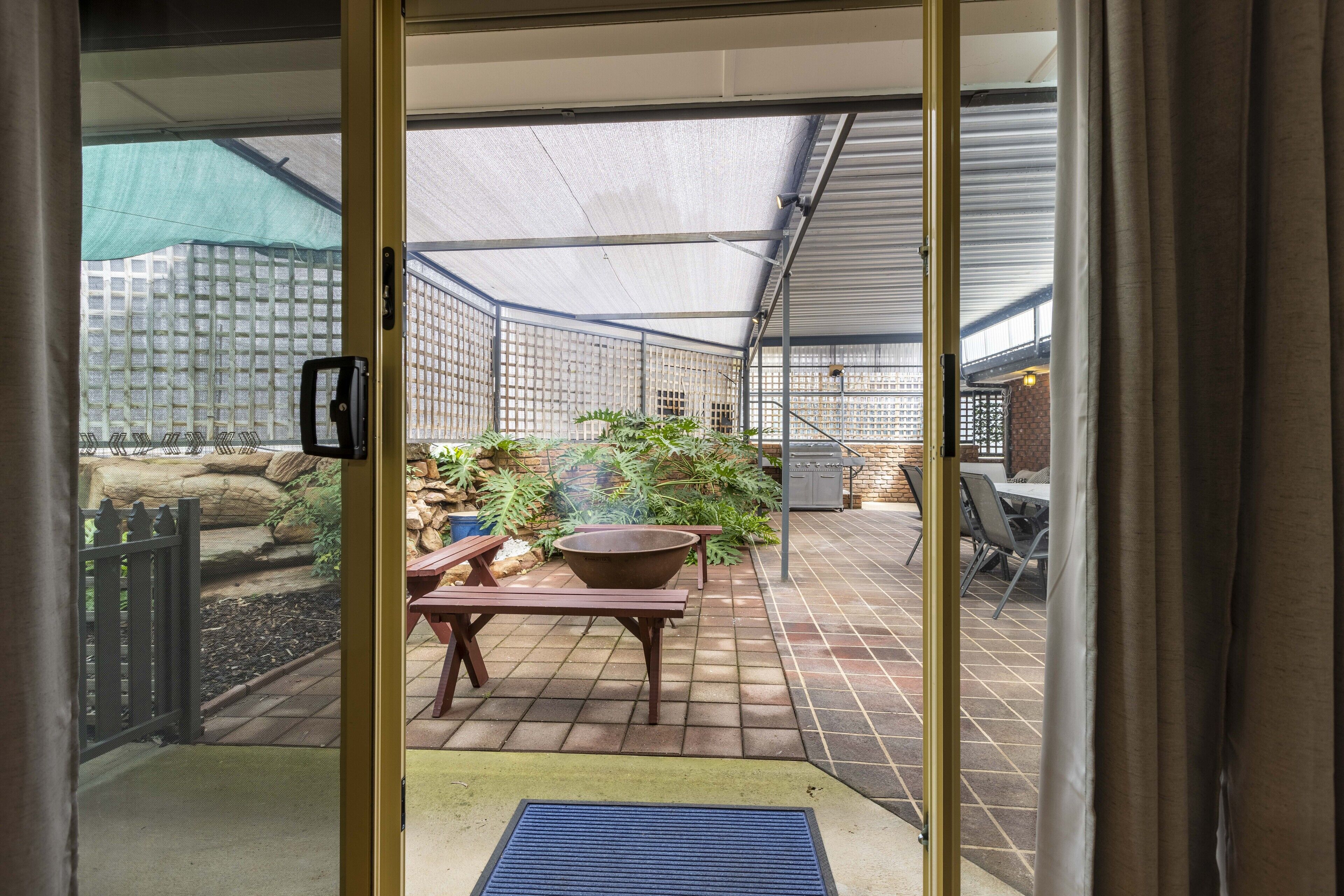 A patio area with a covered seating area, a fire pit, and a view of the surrounding garden.