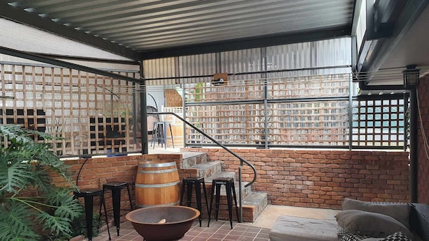 Un patio cubierto con paredes de ladrillo, un barril de madera, una mesa redonda y un sofá.