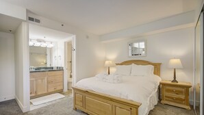 A bedroom with a wooden bed, bedside lamps, a nightstand, a mirror, and a bathroom with a vanity and sink. - Empire Coalition Ski Condo - Walking distance to PC Mtn - Free bus route (Park City)