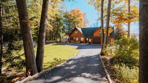 A two-story house with a garage, surrounded by trees and a well-maintained lawn. - Waterfront, Hot Tub, 9 Beds - Wildwood Lakehouse (Interlochen)