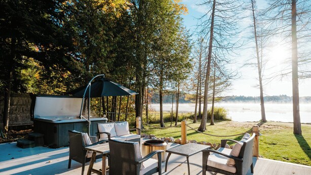 An outdoor patio with wicker furniture, a grill, and a view of a lake. - Waterfront, Hot Tub, 9 Beds - Wildwood Lakehouse (Interlochen)