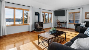 A spacious living room with large windows, a fireplace, a flat-screen TV, and a cozy seating area. - Waterfront, Hot Tub, 9 Beds - Wildwood Lakehouse (Interlochen)
