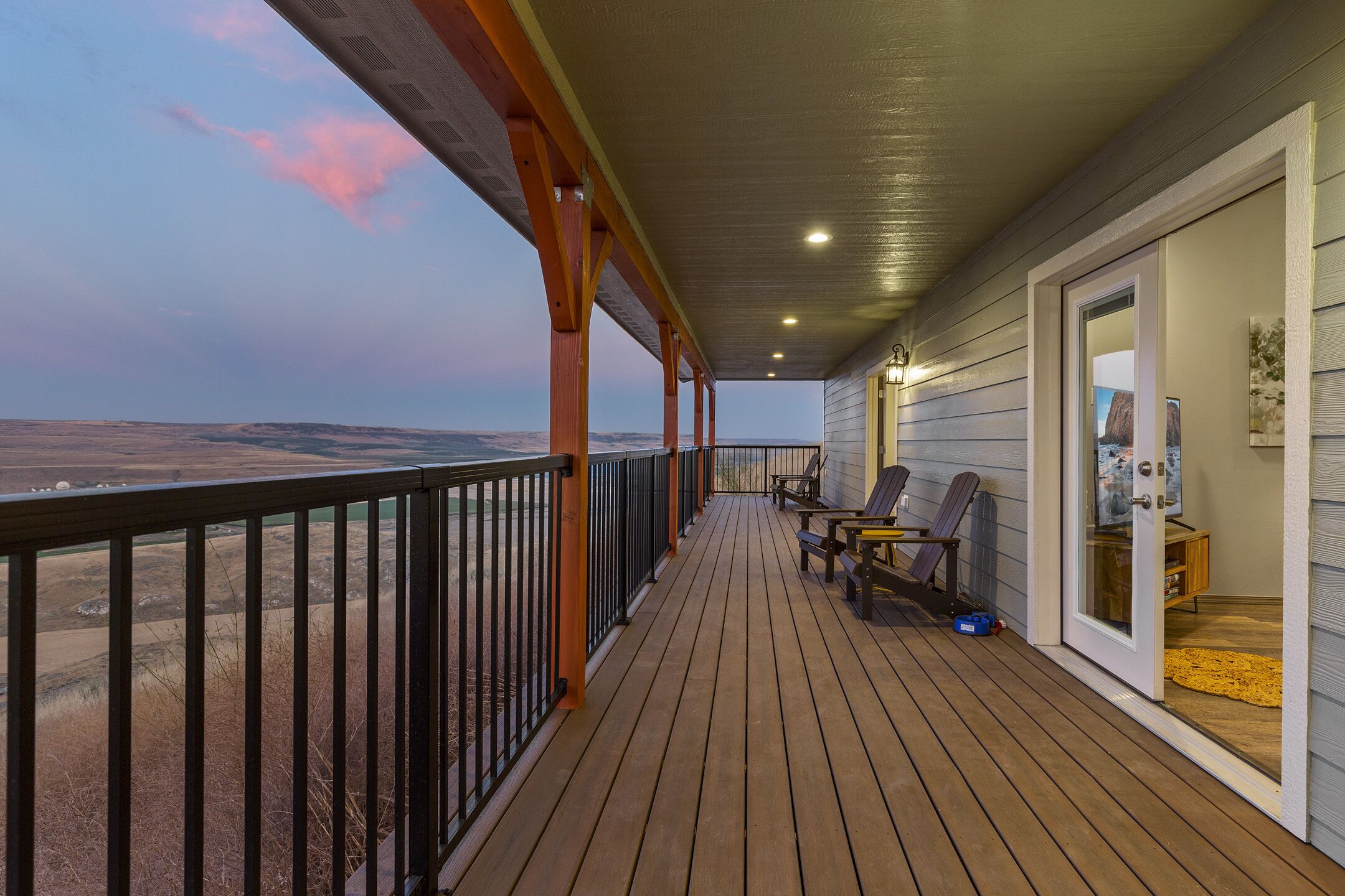 A wooden deck with a view of the landscape, a covered area with chairs, and a door leading to an interior space.