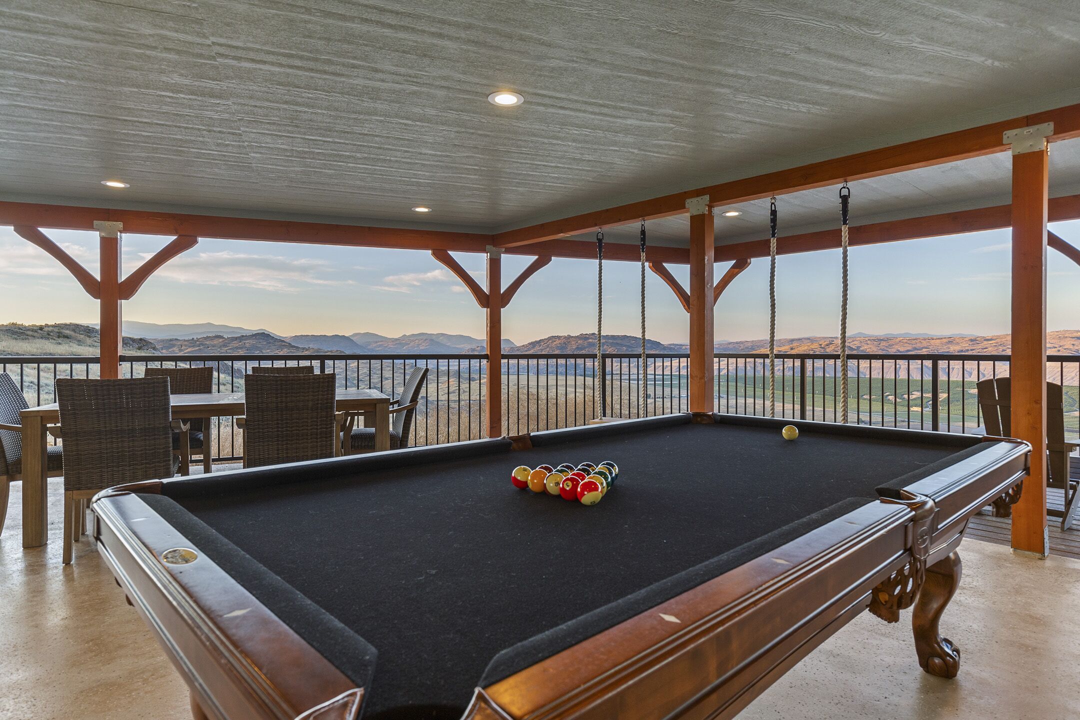 Una mesa de billar con bolas, un área de estar con sillas y mesas, y vistas a montañas.