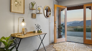 Ein Zimmer mit einem Holztisch, einer Stehlampe, einem Spiegel und Blick ins Freie.