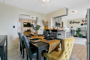 A dining area with a table set for four, surrounded by chairs, and a kitchen area with a 'Welcome' sign. - 3 Miles from Hope Mills Lake! 2 acre home with 5 SmartTvs + Self Check (Hope Mills)