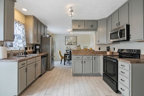A modern kitchen with light grey cabinets, a stainless steel refrigerator, a microwave, and a built-in oven. - 3 Miles from Hope Mills Lake! 2 acre home with 5 SmartTvs + Self Check (Hope Mills)