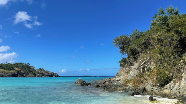 Uma praia com águas turquesa cristalinas, costa rochosa e vegetação exuberante.