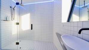 A modern bathroom with a glass-enclosed shower, a white sink, and a large mirror. - Quarters A2- Luxurious studio (Dunedin)