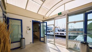 Entrada techada a un puerto deportivo con puertas de vidrio, un cubo de basura y vistas a barcos.