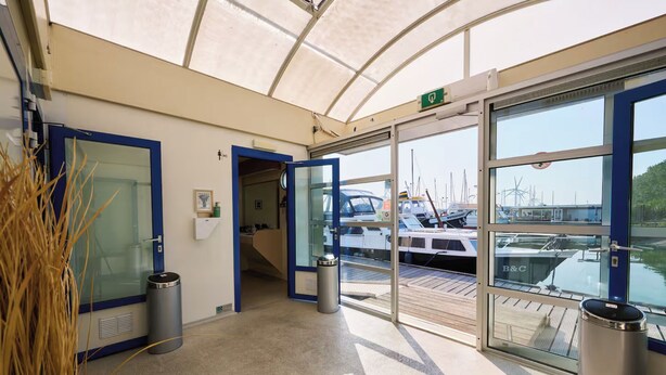 A covered entrance to a marina with glass doors, a trash bin, and a view of boats.