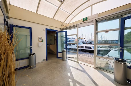 A covered entrance to a marina with glass doors, a trash bin, and a view of boats.