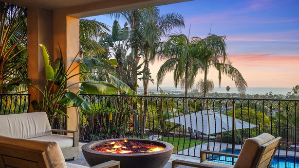 Ein Balkon mit Feuerstelle, Sitzgelegenheiten im Freien und Blick auf das Meer und Palmen.