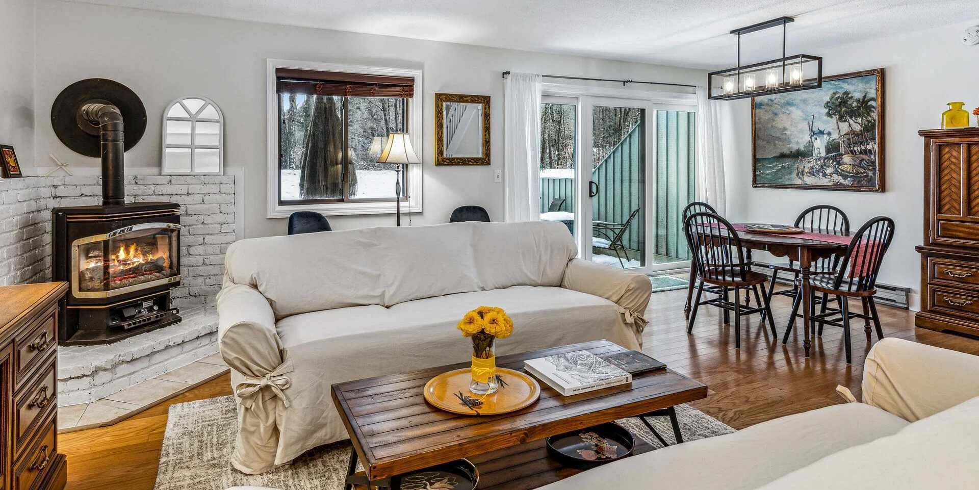A cozy living room with a sofa, a coffee table with a vase, a fireplace, and a dining area with chairs and a table.