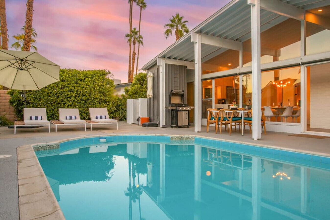 A modern outdoor pool area with lounge chairs, a barbecue grill, and a dining area with a table and chairs.