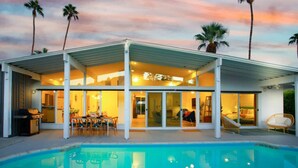 Une maison moderne dotée d’une piscine, de grandes portes vitrées et d’un patio couvert.