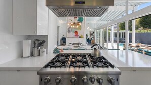 Une cuisine moderne équipée d’une cuisinière à gaz, de meubles blancs et offrant une vue sur une piscine et un espace de détente extérieur.