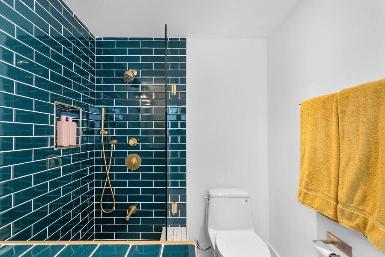 A bathroom with a blue-tiled shower area, a white toilet, and a yellow towel hanging on the wall.