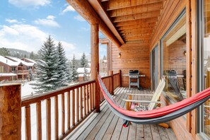 Une terrasse en bois avec un hamac, un barbecue et une vue sur des arbres couverts de neige.