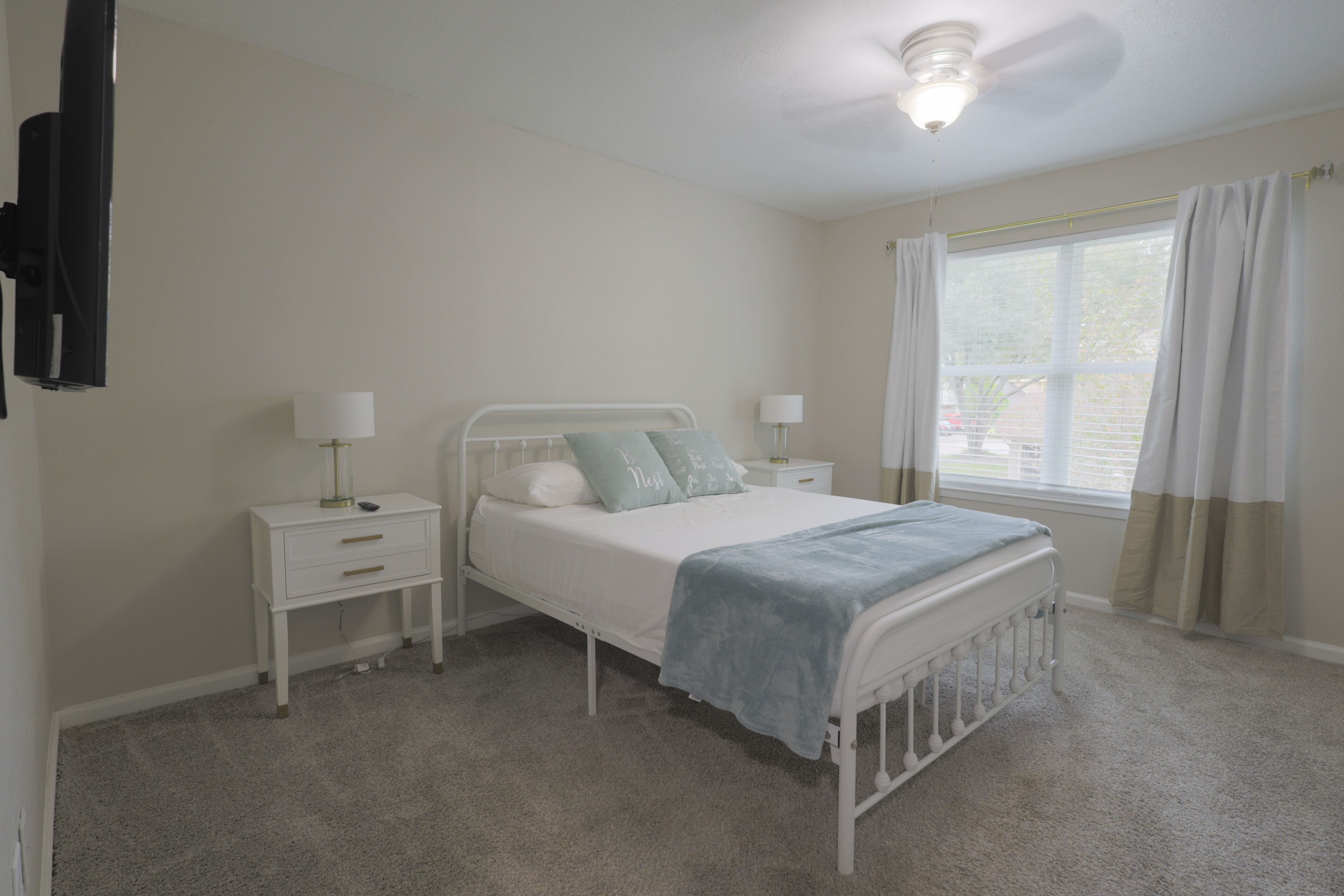 A bedroom with a single bed, bedside tables, a ceiling fan, and a window with curtains.