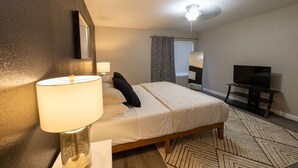 Una camera d'albergo con un letto, una lampada, una televisione e una ventola a soffitto.