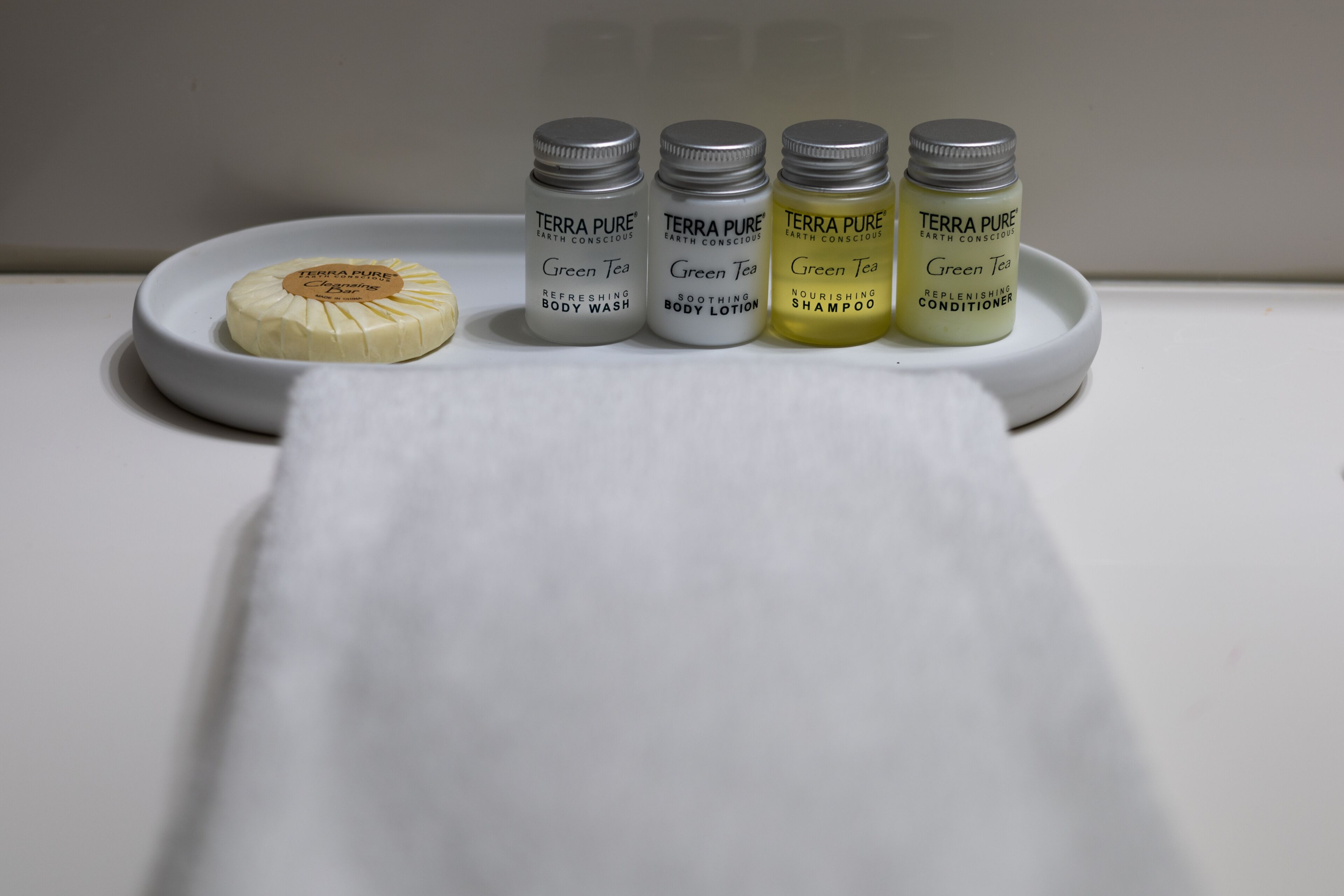 Quatre flacons de gel douche, de lotion et de shampoing Terra Pure Green Tea, présentés sur une assiette blanche.