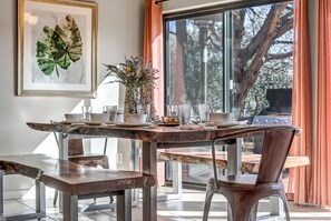 A dining area with a rustic wooden table, metal chairs, and a large window with orange curtains. - Spacious 3BR Sedona villa with forest views, patio, Wi-Fi, and garage. (Sedona)